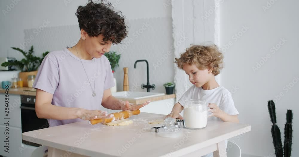 Happy girl and little son are rolling dough making cookies at home in kitchen sitting at table busy with activity. Young family, household and food concept. Happy girl and little son are rolling dough making cookies at home in kitchen sitting at table busy with activity. Young family, household and food concept.
