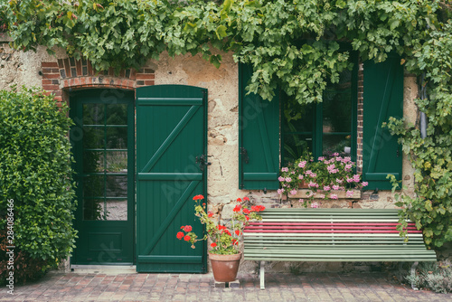 beautiful tradiitional little french house entrance and facade surronded by beautiful picturesque tradiitional little french house entrance and facade surronded by vine anf flowerswith a bench outside photo
