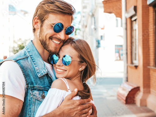Smiling beautiful girl and her handsome boyfriend. Woman in casual summer dress and man in jeans clothes. Happy cheerful family. Female having fun on the street background.Hugging couple in sunglasses