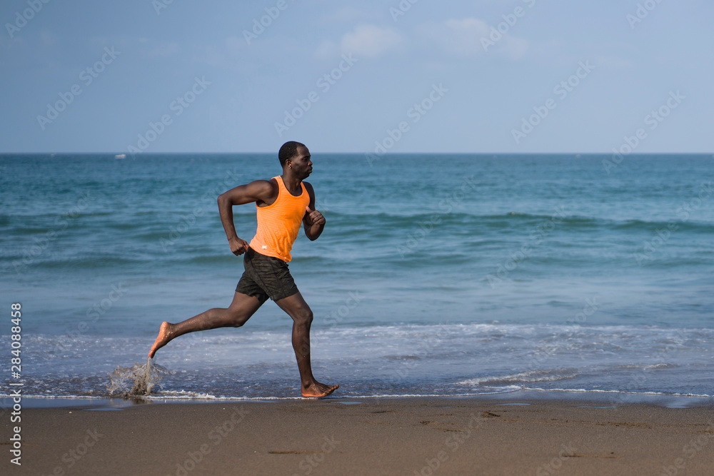 athletic full body portrait of young attractive and fit black afro American man running on the beach doing Summer fitness jogging workout at the sea in healthy lifestyle concept athletic full body portrait of young attractive and fit black afro American man running on the beach doing Summer fitness jogging workout at the sea in healthy lifestyle concept
