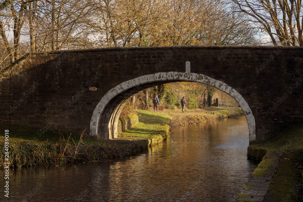 Fototapeta premium The bridge over the canal at Dowley Gap frames walkers on the towpath during an autumnal walk