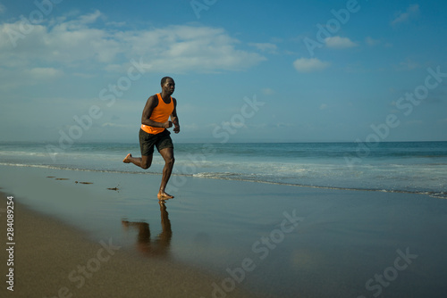athletic full body portrait of young attractive and fit black afro American man running on the beach doing Summer fitness jogging workout at the sea in healthy lifestyle concept