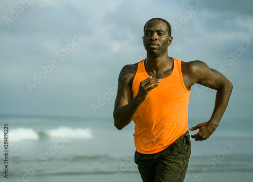 young attractive and fit black African American man running on the beach doing Summer fitness jogging workout at the sea in sport exercise and healthy lifestyle concept
