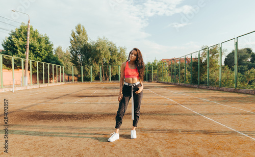 Fotografia Stylish  girl in street clothes standing on an old tennis court and posing at camera