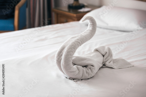 Fototapeta Naklejka Na Ścianę i Meble -  Beautiful swan from white bath towel decorate on bed corner and soft sunlight in background, nice greeting from Hotel.