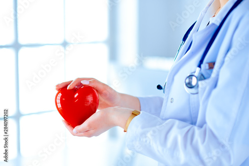 Female doctor with stethoscope holding heart, on light background. Health, medicine, people and cardiology concept photo