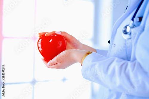 Female doctor with stethoscope holding heart, on light background. Health, medicine, people and cardiology concept