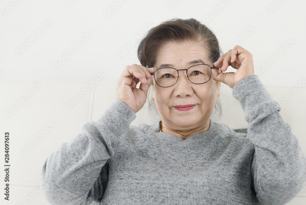 Happy Asian senior woman wearing eyeglasses and sitting on sofa at home, lifestyle concept. Happy Asian senior woman wearing eyeglasses and sitting on sofa at home, lifestyle concept.