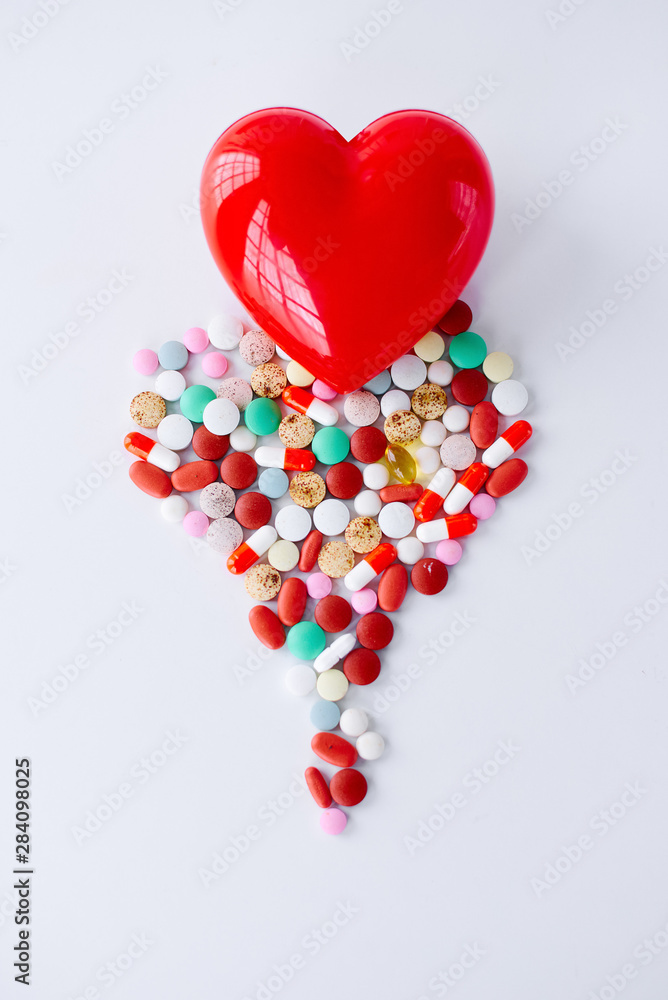 Multicolored pills on a table in the shape of a heart on a white background. Red heart . Doctor's hands on the table near the heart and pills. Top view with copy space. Medicine concept