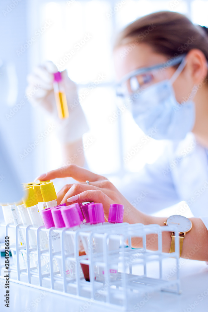 Female scientist explore a test tube with liquid in a laboratory. Researcher is surrounded by medical vials and flasks Female scientist explore a test tube with liquid in a laboratory. Researcher is surrounded by medical vials and flasks