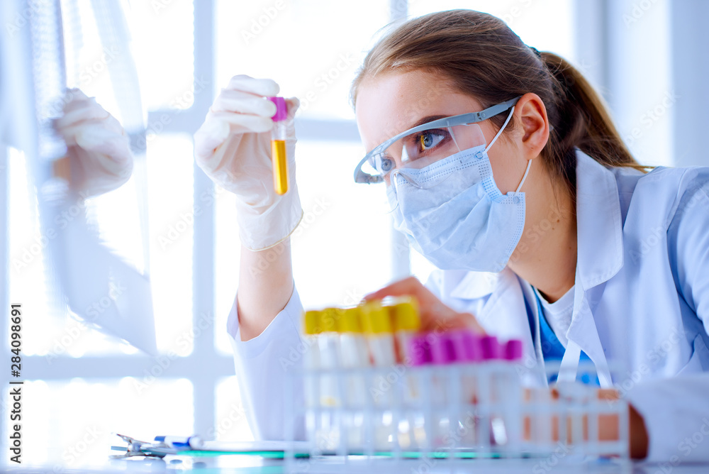 Female scientist explore a test tube with liquid in a laboratory. Researcher is surrounded by medical vials and flasks Female scientist explore a test tube with liquid in a laboratory. Researcher is surrounded by medical vials and flasks
