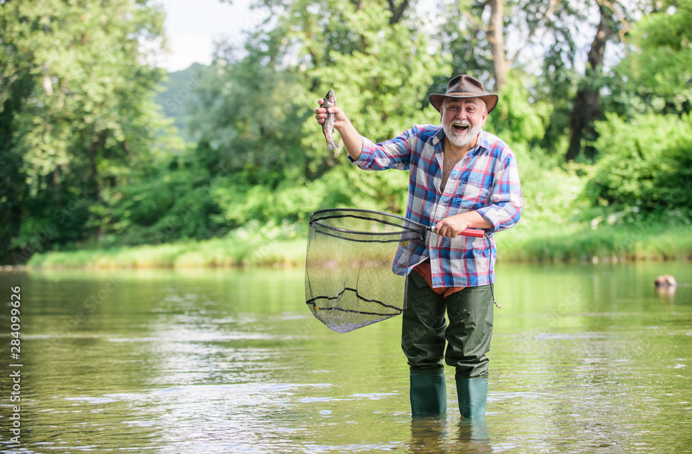 Fisherman fishing equipment. Hobby sport activity. Pensioner leisure. Fish farming pisciculture raising fish commercially. Fisherman alone stand in river water. Man senior bearded fisherman