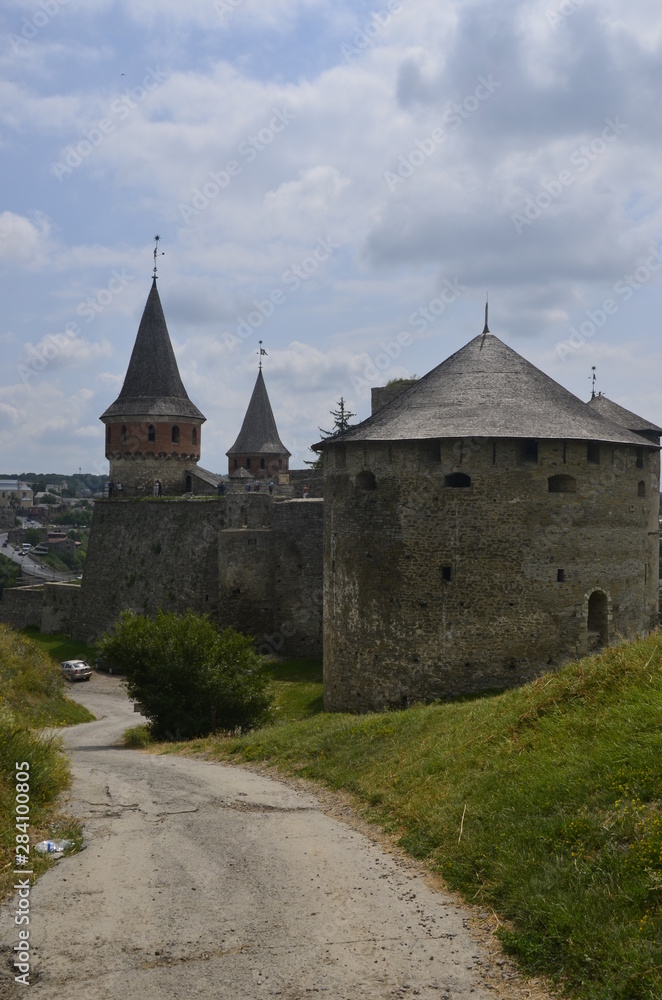 Castle on the hill. The wall and towers of the magic fortress in Kamyanets-Podilsky in Ukraine against the background of a blue-haired sky and green grass