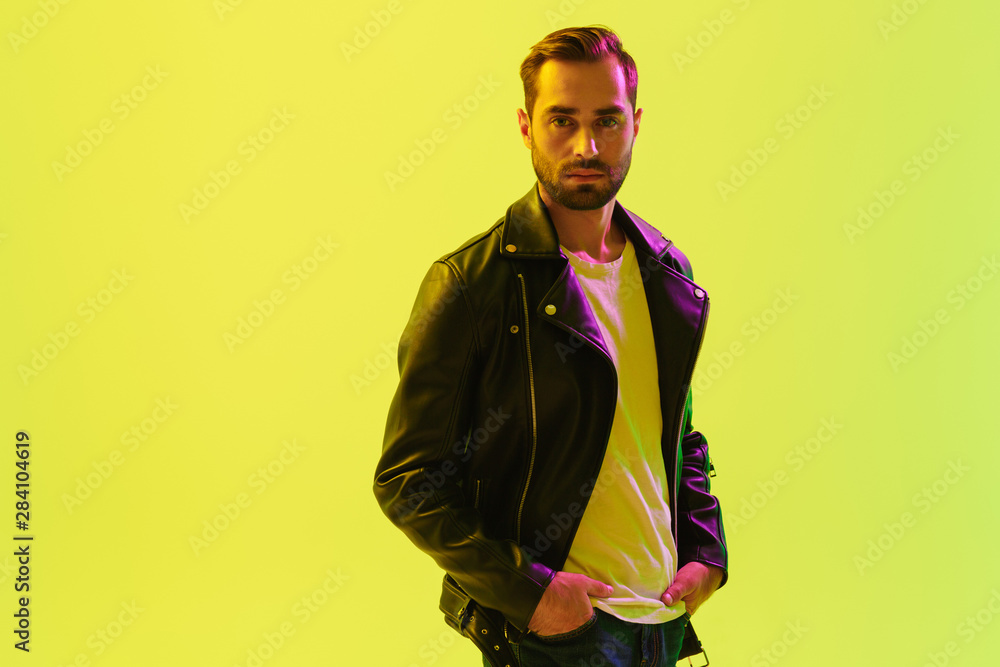Handsome young stylish man posing isolated over light green background wall with led neon lights dressed in leather jacket. Handsome young stylish man posing isolated over light green background wall with led neon lights dressed in leather jacket.
