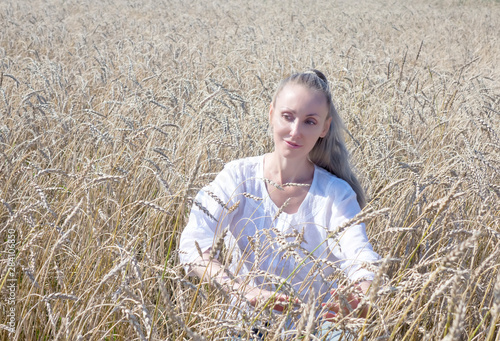 portrait of a beautiful young woman in a white blouse with long blond hair in a field of golden wheat ears on a summer day