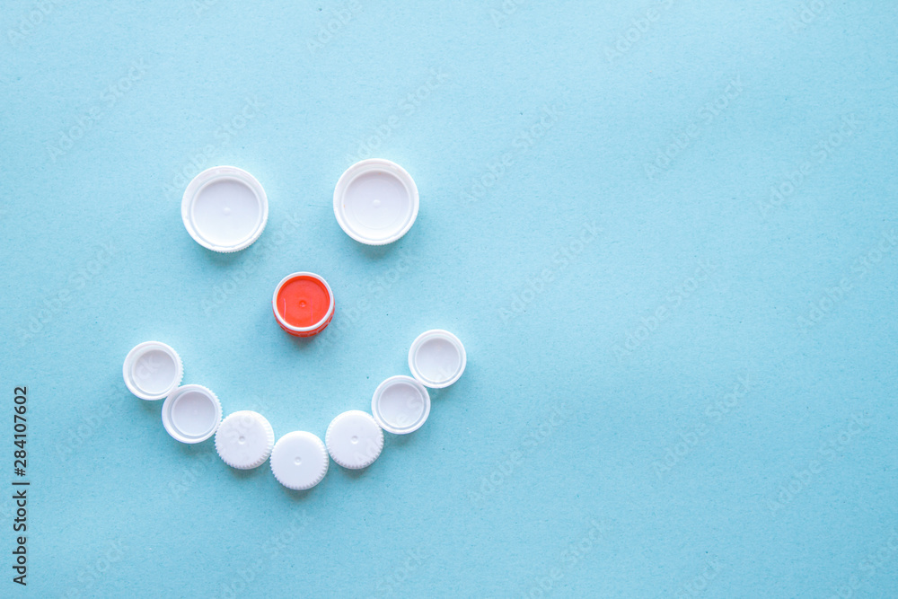 Smiley face from bottle caps. Collection of plastic waste on a blue background. The concept of plastic recycling and the environment. Flat position, top view Smiley face from bottle caps. Collection of plastic waste on a blue background. The concept of plastic recycling and the environment. Flat position, top view