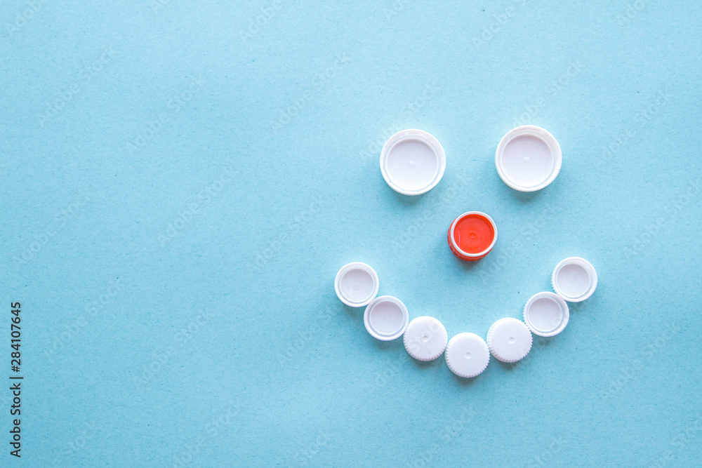 Smiley face from bottle caps. Collection of plastic waste on a blue background. The concept of plastic recycling and the environment. Flat position, top view Smiley face from bottle caps. Collection of plastic waste on a blue background. The concept of plastic recycling and the environment. Flat position, top view