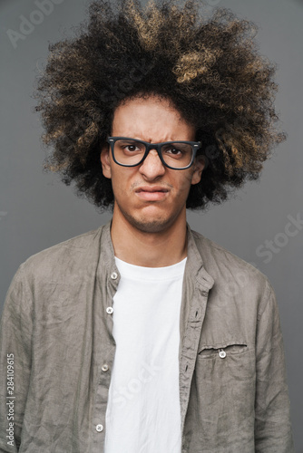 Young curly displeased guy posing isolated over grey wall background.