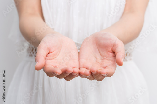 Woman hands cupped together against white dress.