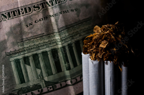 Numerous isolated tobacco cigarettes with shredded tobacco on top of them on a background with a five dollar bill. Tobacco can cause diseases. photo