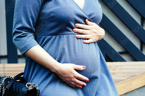 Belly of a pregnant woman in a blue elegant dress with lurex.