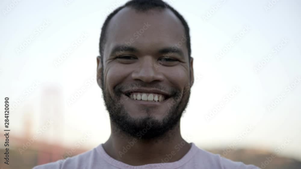Handsome man smiling at camera. Close-up portrait of cheerful young African American man posing with hand on chin and looking at camera outdoor. Emotion concept Handsome man smiling at camera. Close-up portrait of cheerful young African American man posing with hand on chin and looking at camera outdoor. Emotion concept