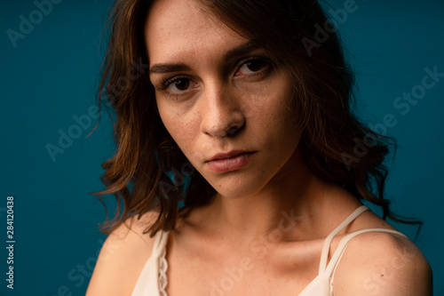 Portrait of young European female with healthy clean skin and blue eyes wearing casual top looking at camera with serious expression. Caucasian woman model with hair gathered in bunch posing indoors