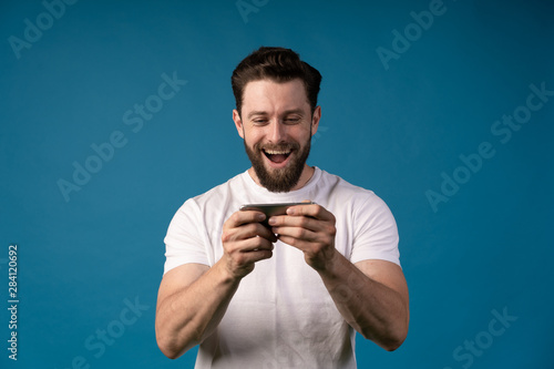 Businessman using mobile phone app texting outside of office blue background. Young caucasian man holding smartphone for business work.