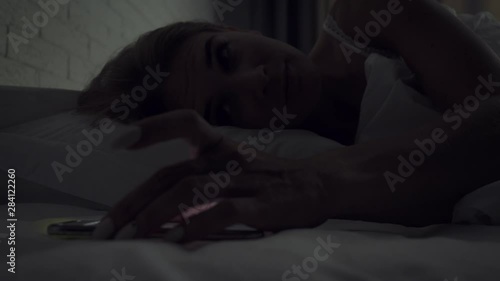 Sleepy woman turns alarm off while awakening in the morning.