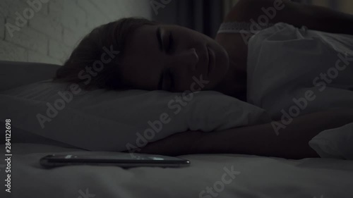 Sleepy woman turns alarm off while awakening in the morning.