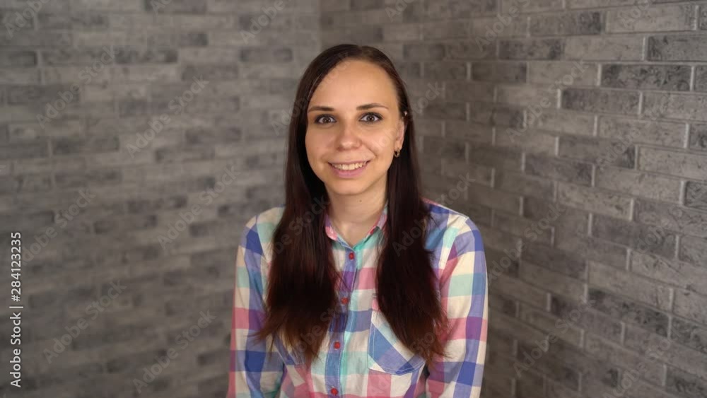 A beautiful young woman in plaid shirt laughs happily and expresses positive emotions on a brick background. A beautiful young woman in plaid shirt laughs happily and expresses positive emotions on a brick background.