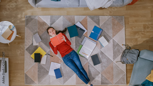 Photos Young Girl in Red Coat and Blue Jeans is Lying Down on a Floor, Reading a Notebook