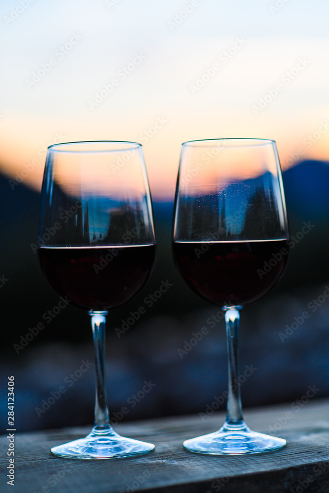 Two glasses of wine at sunset dramatic sky on mountain landscape background