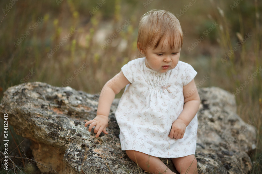 Beautiful little baby girl sitting in nature. Look down. The concept is tenderness, naivety, simplicity.