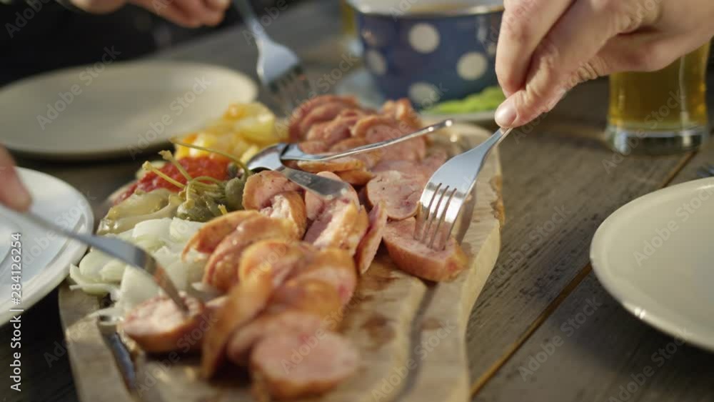 Slow motion, close up friends sit at the picnic table and eat sausage and vegetable on the wooden cutting board