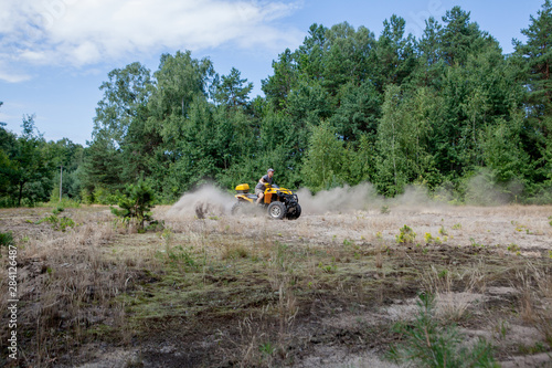 Man riding a yellow quad ATV all terrain vehicle on a sandy forest. Extreme sport motion, adventure, tourist attraction.
