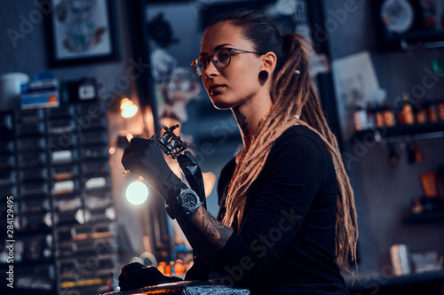 Foto Pretty expirienced tattoo artist in glasses is tuning her new tattoo machine before tattooing session