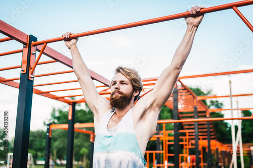 strong athlete doing pull-up on horizontal bar. Muscular man doing pull ups on horizontal bar in park. Gymnastic Bar During Workout. training strongmanoutdoor park gym. Man Doing Exercise gym Outdoor