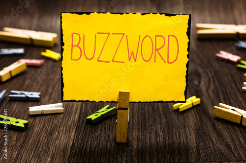 Handwriting text Buzzword. Concept meaning Fashionable word Commonly very often used expression Popular Clothespin holding yellow paper note several clothespins wooden floor photo