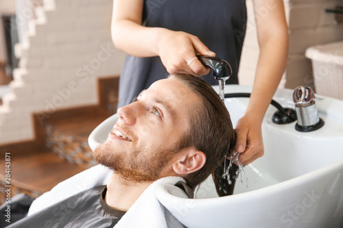 Female hairdresser washing hair of young man in salon