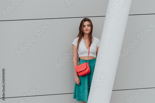 Young women dressed in white topic and turquoise skirt with coral bag, on grey street backgraund. Fashion and stylish concept. photo