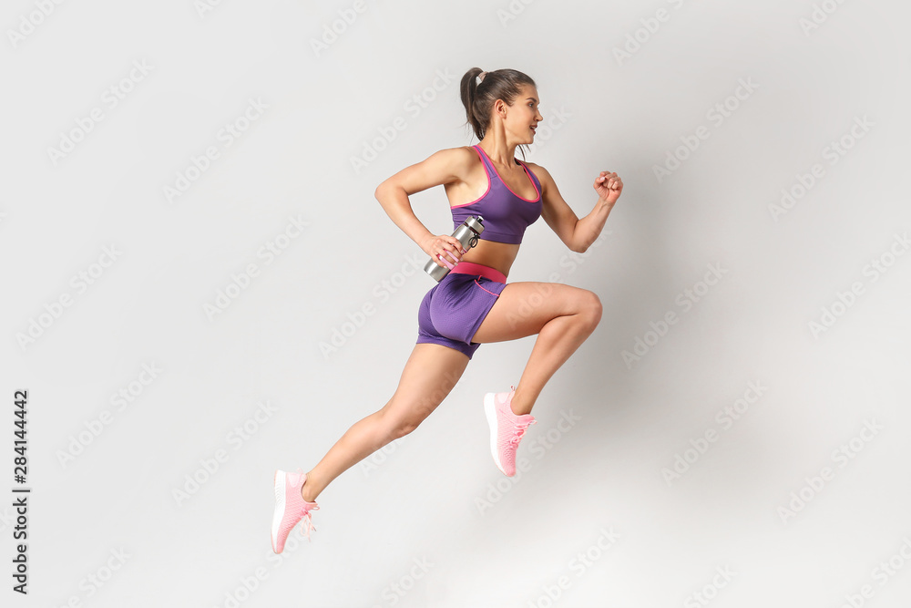 Running sporty woman with bottle of water on light background