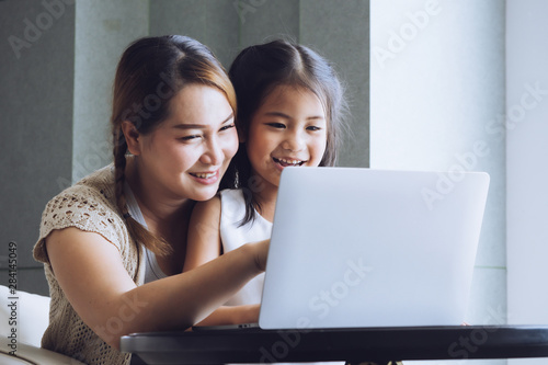 Happy mother with little kid daughter using laptop at home.