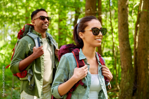 travel, tourism, hike and people concept - mixed race couple walking with backpacks in forest