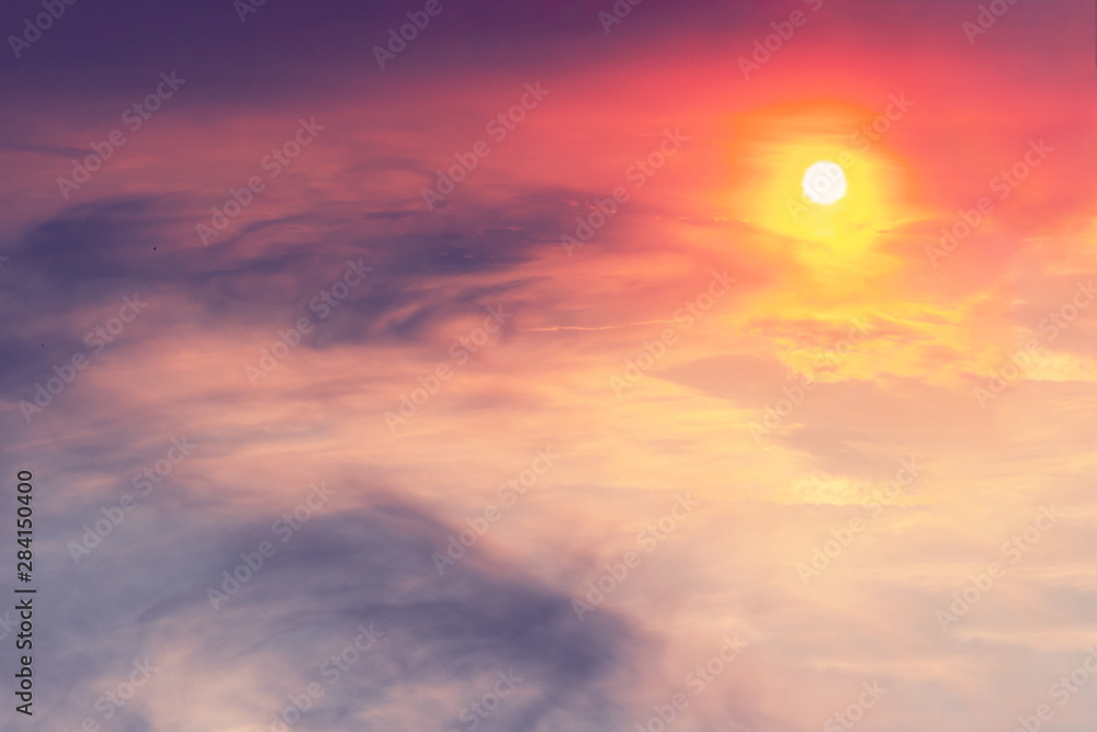 Fototapeta premium The sunset in the sky is pink-orange with purple clouds in the form of stains on which the sun shines. Landscape concept.