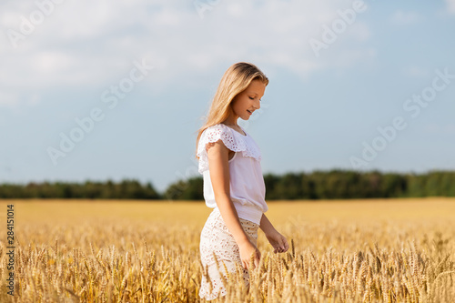 nature, harvest and people concept - smiling young girl on cereal field in summer