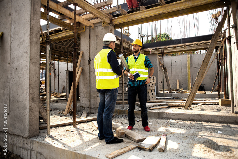 Men in hardhat and green jacket posing on building site. Men in hardhat and green jacket posing on building site.