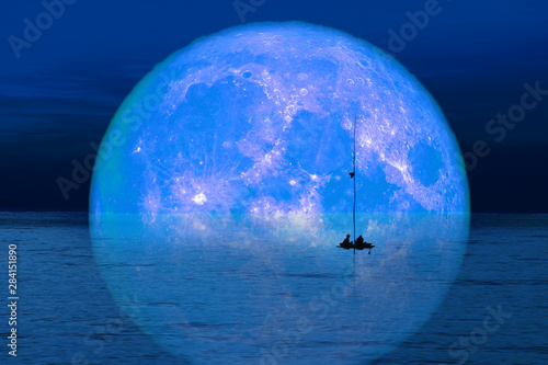 reflection full harvest moon on sky and silhouette men on fishing boat on night sea