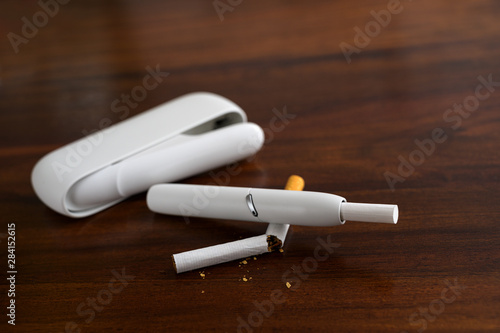 Heating tobacco system is breaking a cigarette on a brown table, the e-cigarette with tobacco sticks generates a nicotine aerosol and allegedly causes harm reduction in smokers, copy space,