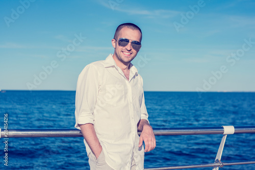 Handsome man in sunglasses stands by the sea and smiles, front view, copy space